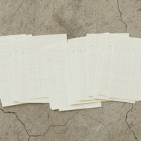 Multiple sheets of white paper with grid lines on a textured beige surface